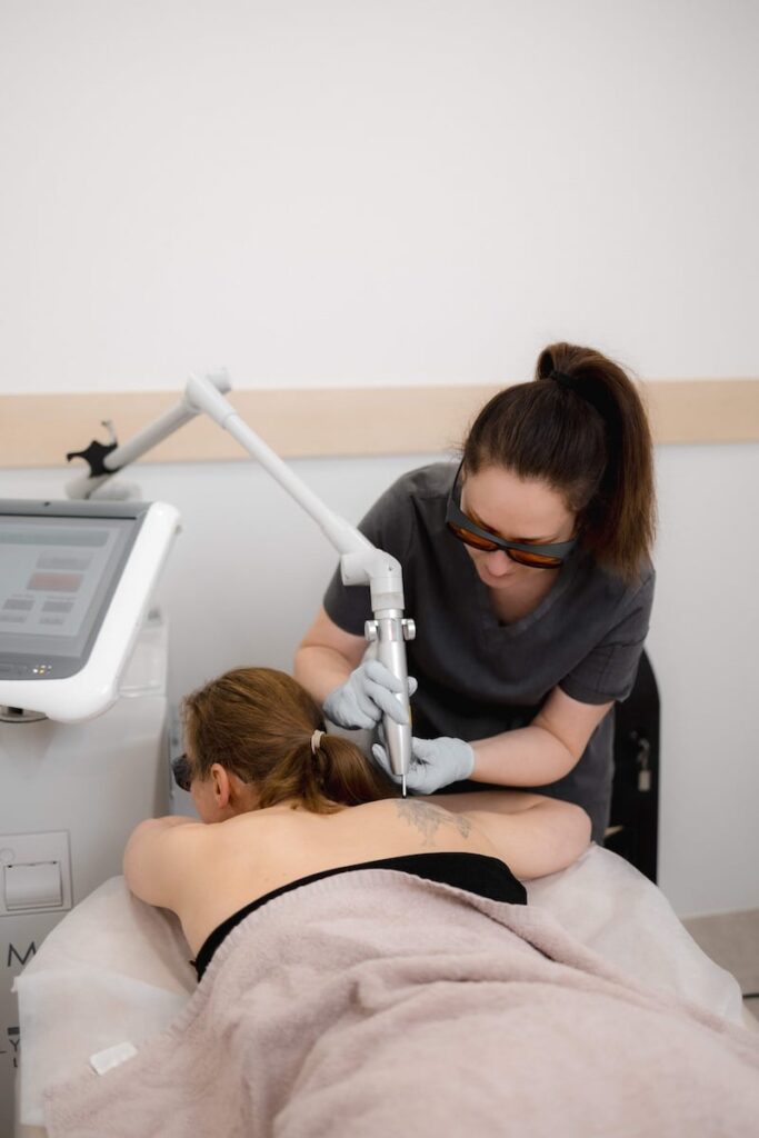 Skinoza Clinic practitioner performing laser tattoo removal on a client’s back, wearing protective laser-safety goggles and using a medical-grade LUMI device