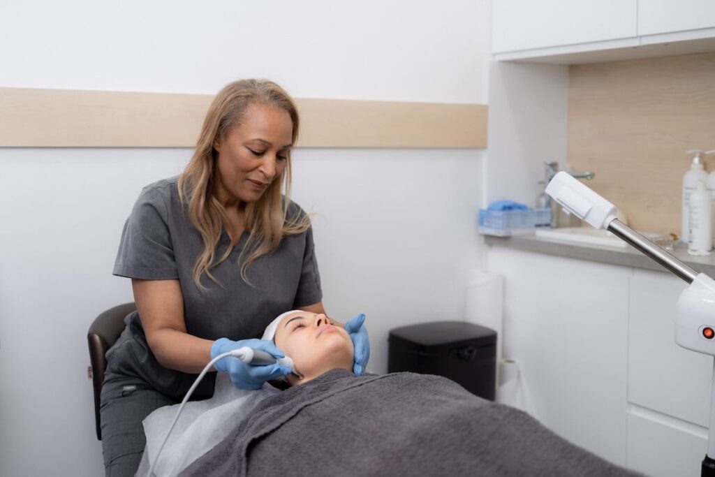 Skinoza Clinic practitioner performing a HydraFacial in London — gentle exfoliation and serum infusion on a brunette client lying on the treatment bed